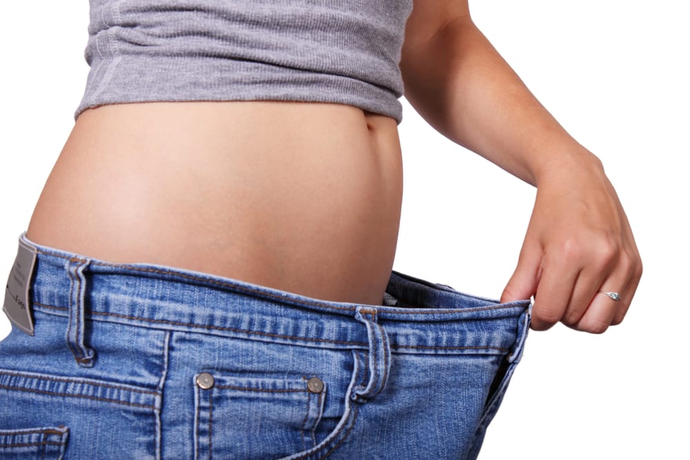 Person holding out loose jeans at the waist to show weight loss progress
