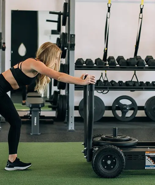Woman pushing weighted sled on turf at STAT Wellness Atlanta functional-training session.