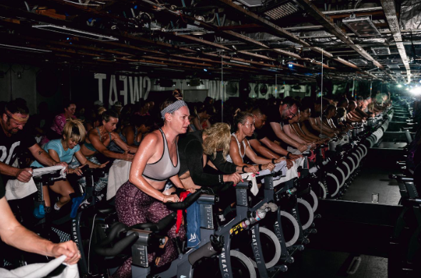 Full class riding in sync with instructor at front of studio at Sweat Cycle Buckhead Atlanta.