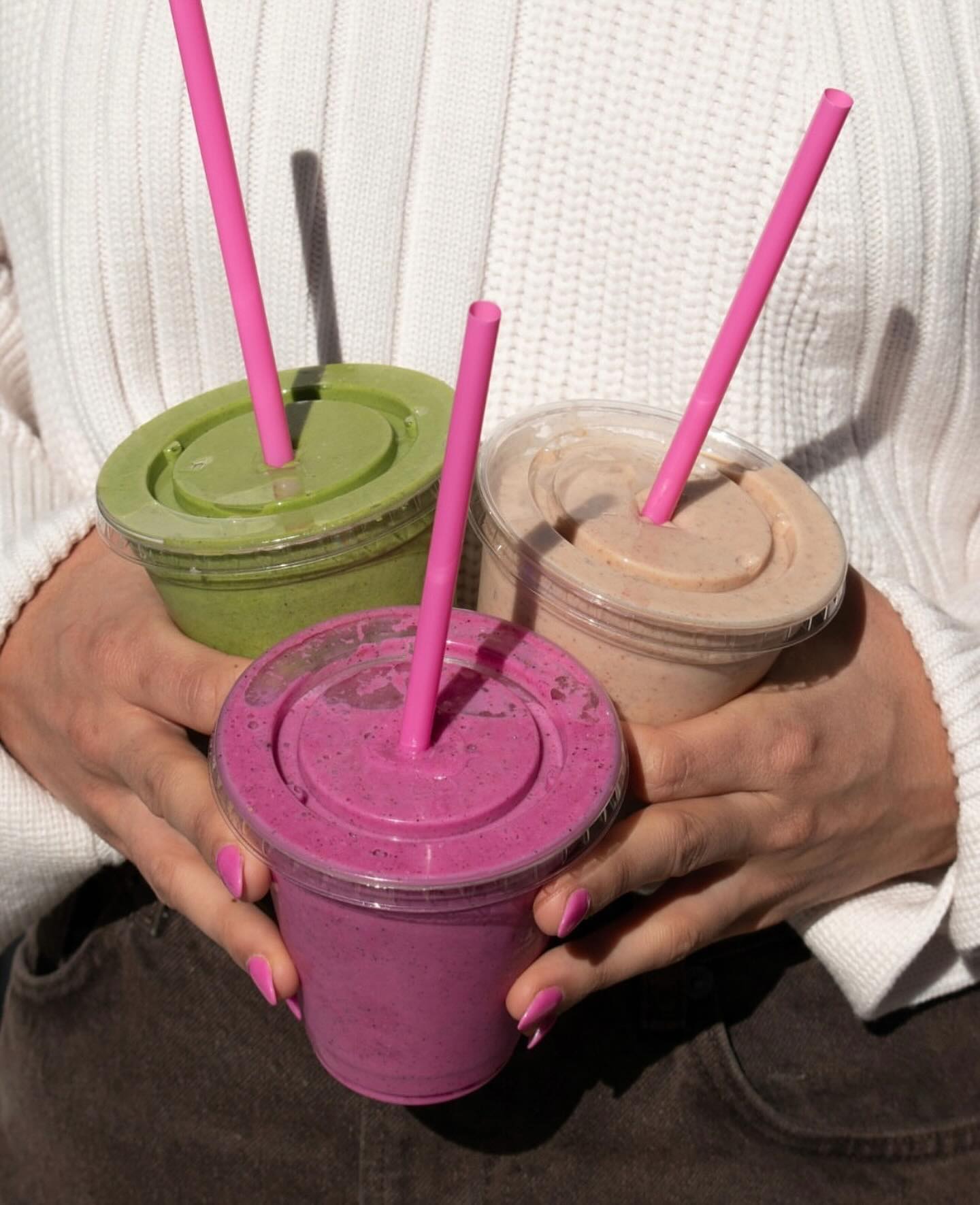 Hand holding bright magenta dragon-fruit smoothie with pink straw.