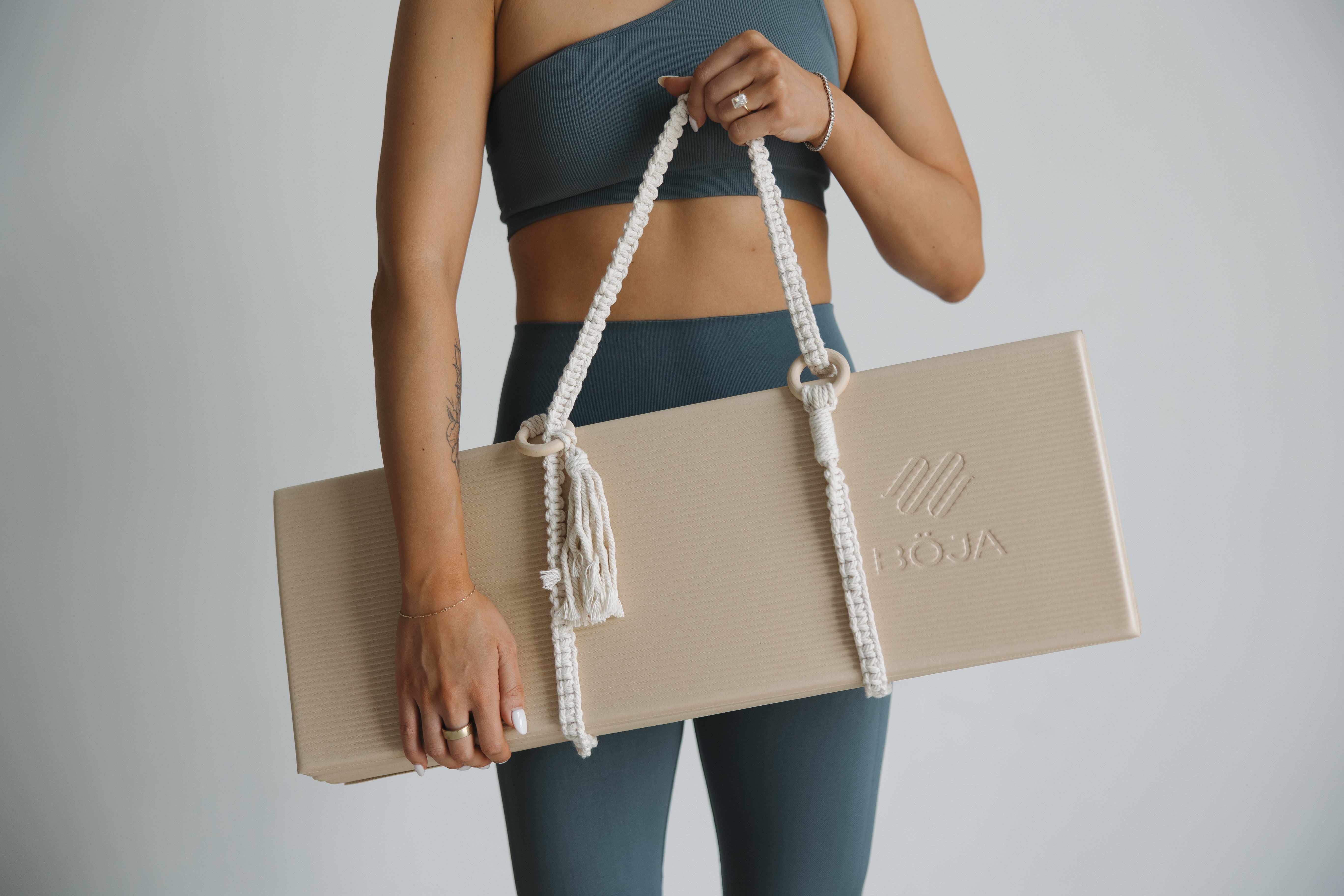 Hand holding compact BOJA foldable yoga mat by strap, showing portable design for travel.