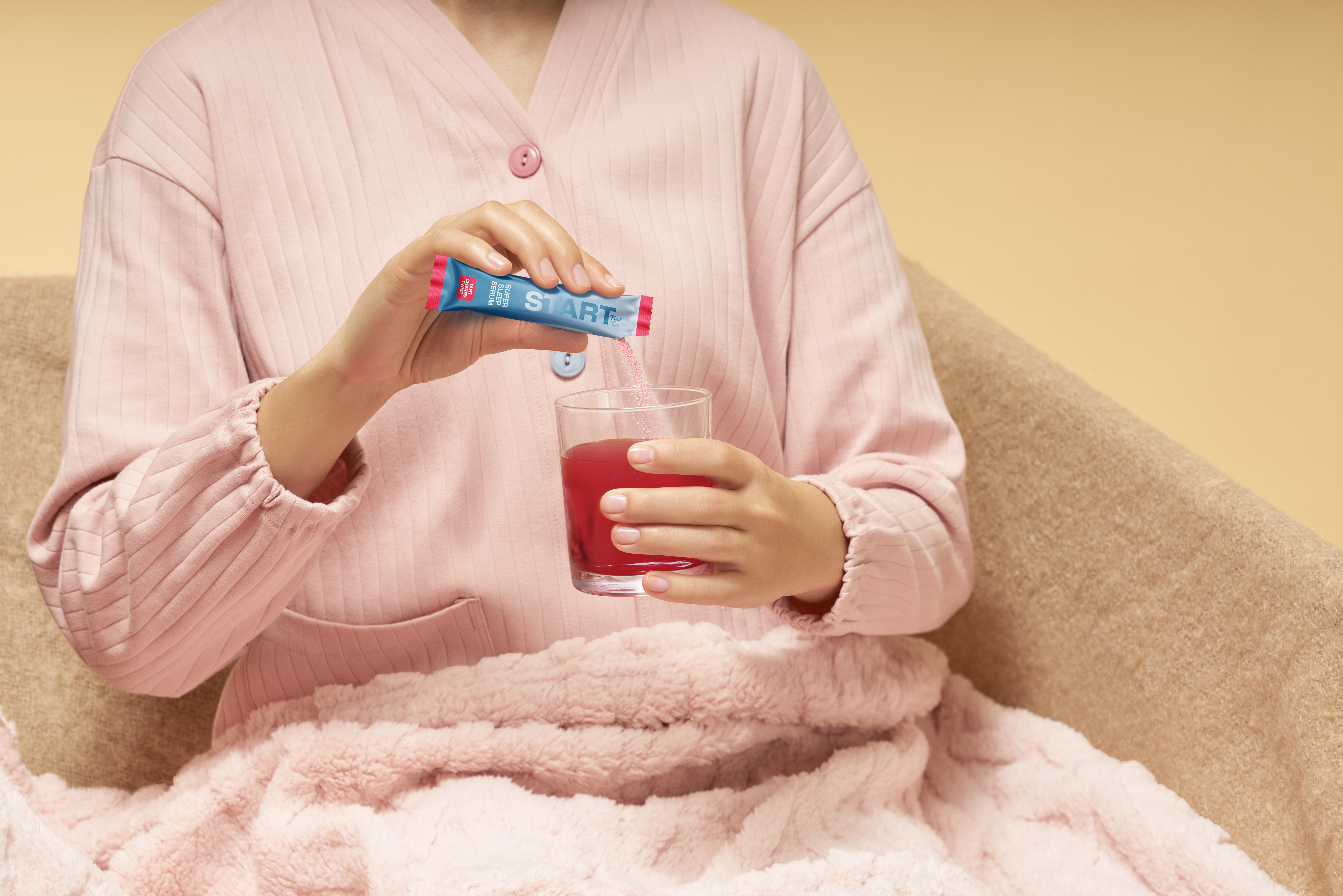 Person in a pink robe pouring a Super Sleep Serum stick into a small red glass.