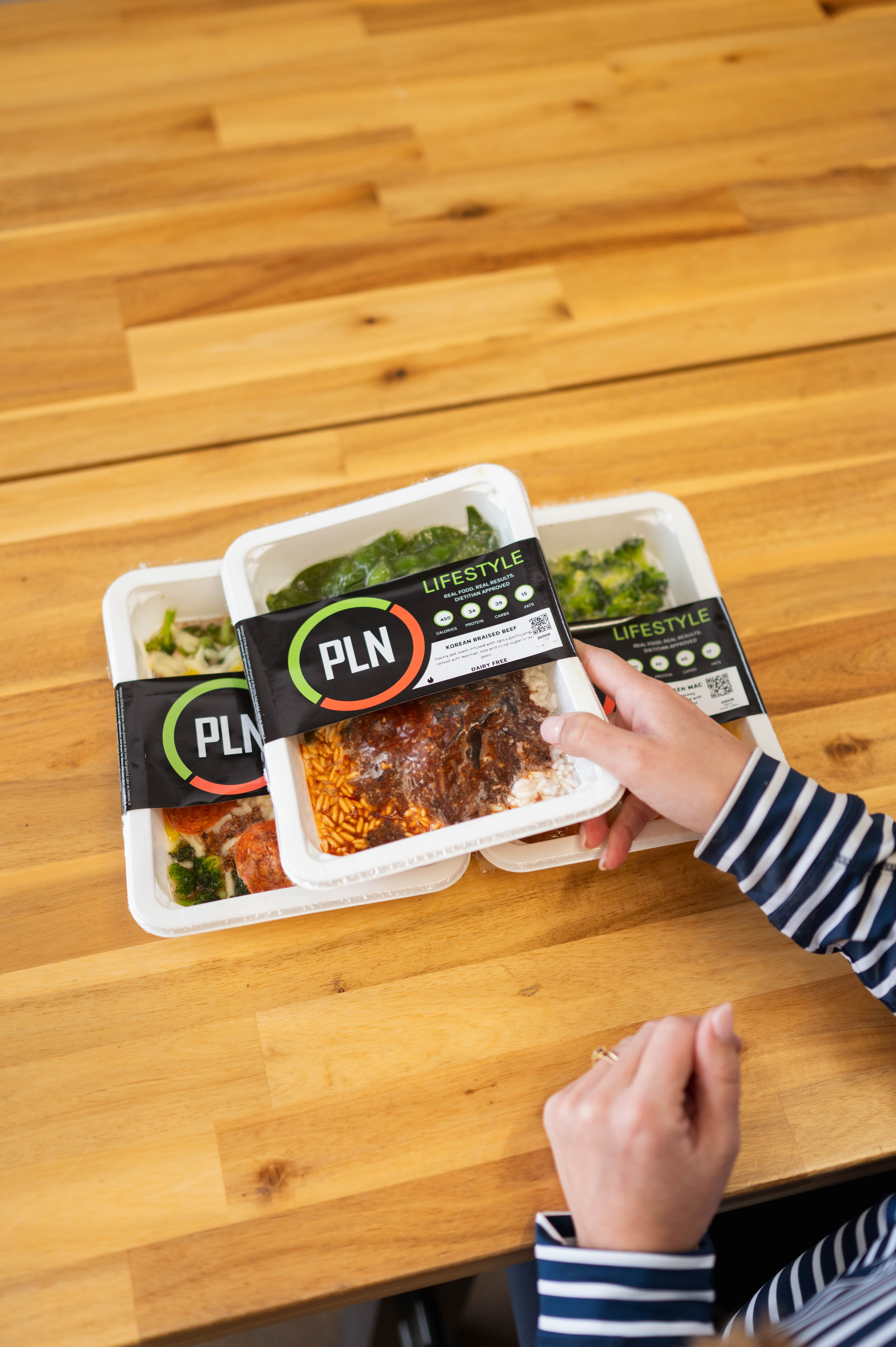 Overhead view of Project LeanNation meal containers with labels on a wooden table in South End Charlotte.