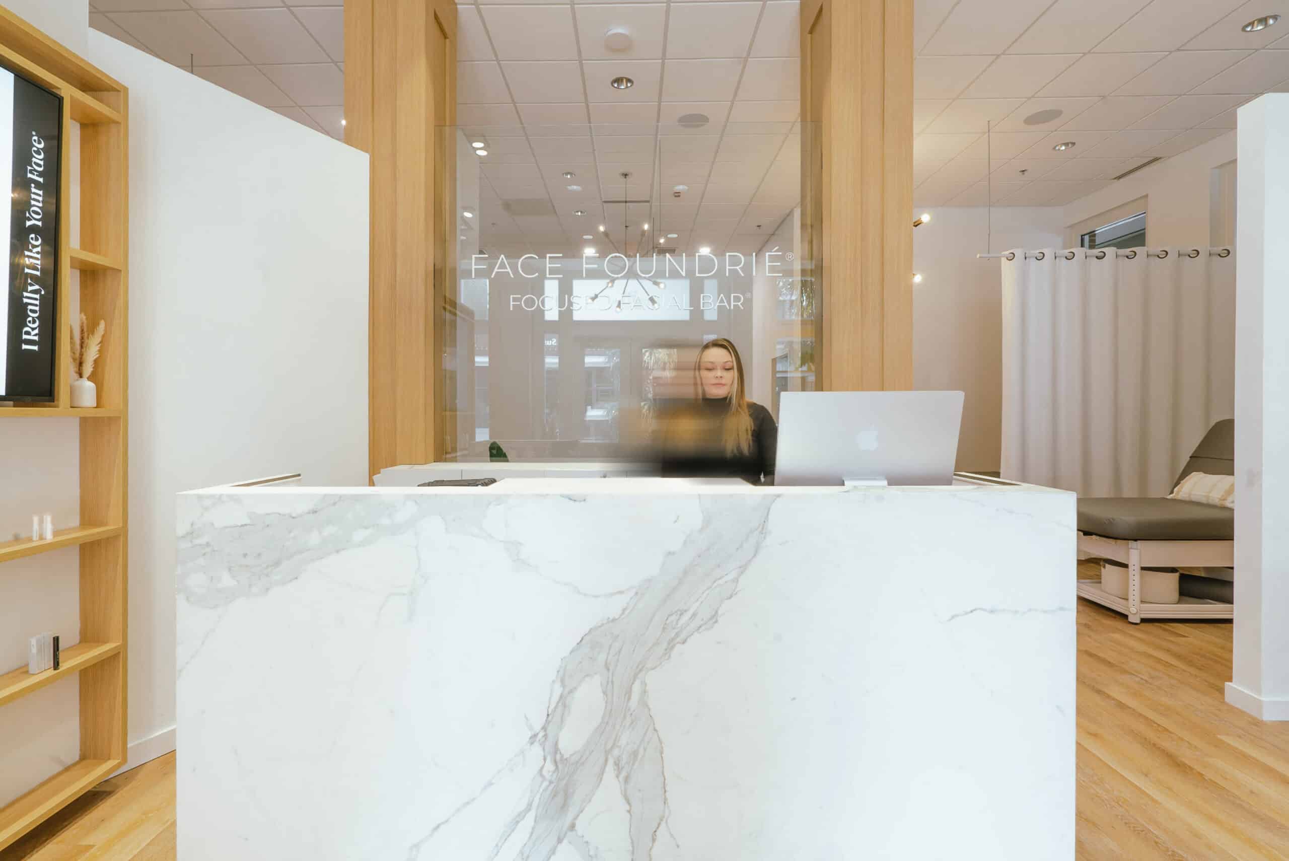 White marble front desk at FACE FOUNDRIÉ Charlotte – South End reception area.