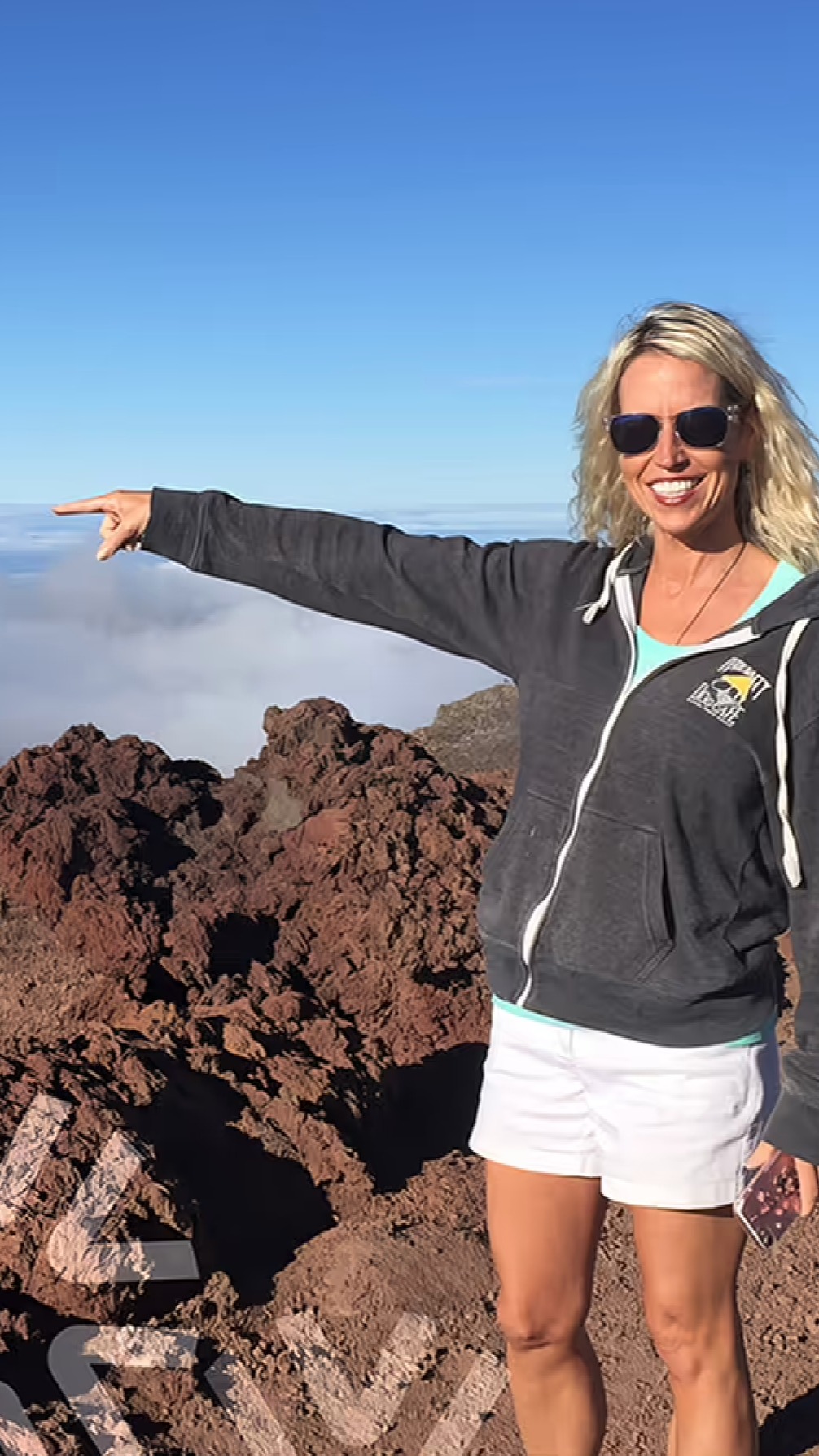 Person in activewear on rocky landscape pointing toward the horizon