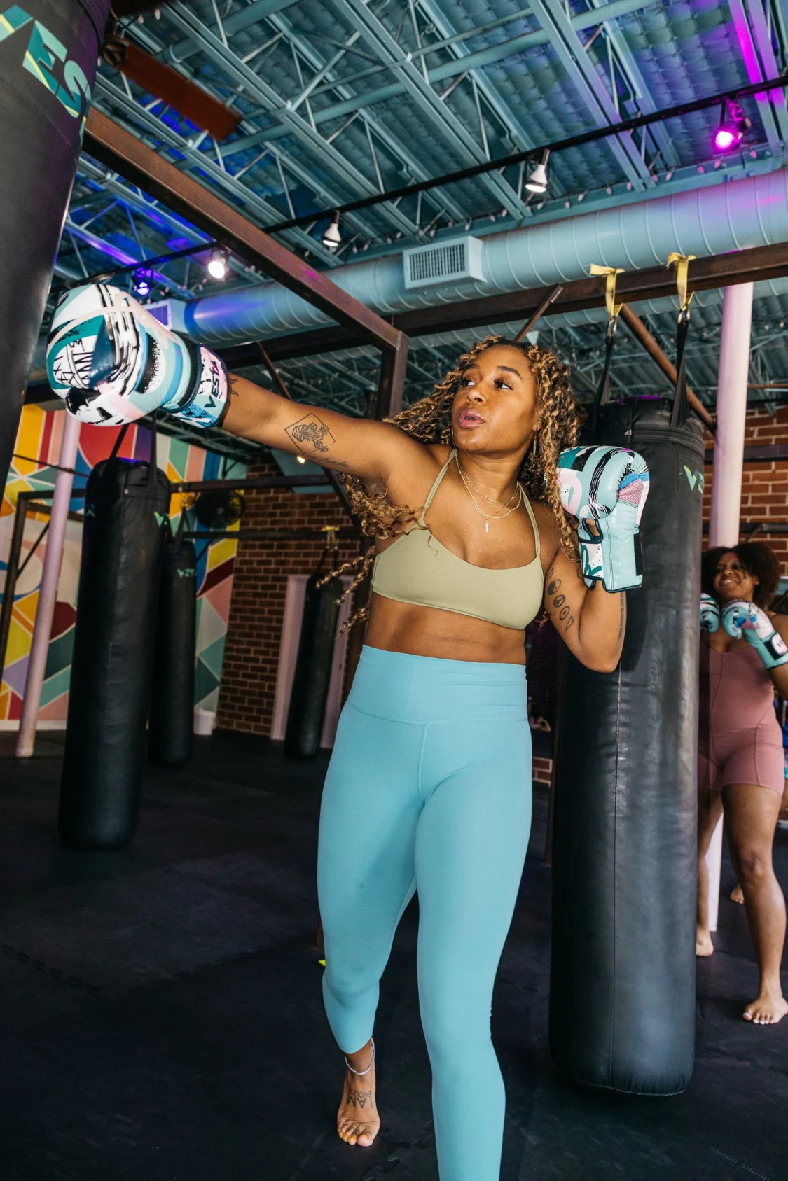 Woman punches heavy bag in blue-pink lights inside VESTA Fitboxing Old Fourth Ward Atlanta.