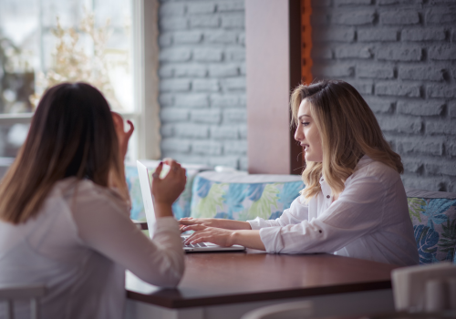 Two women chat in a relaxed setting with a laptop.