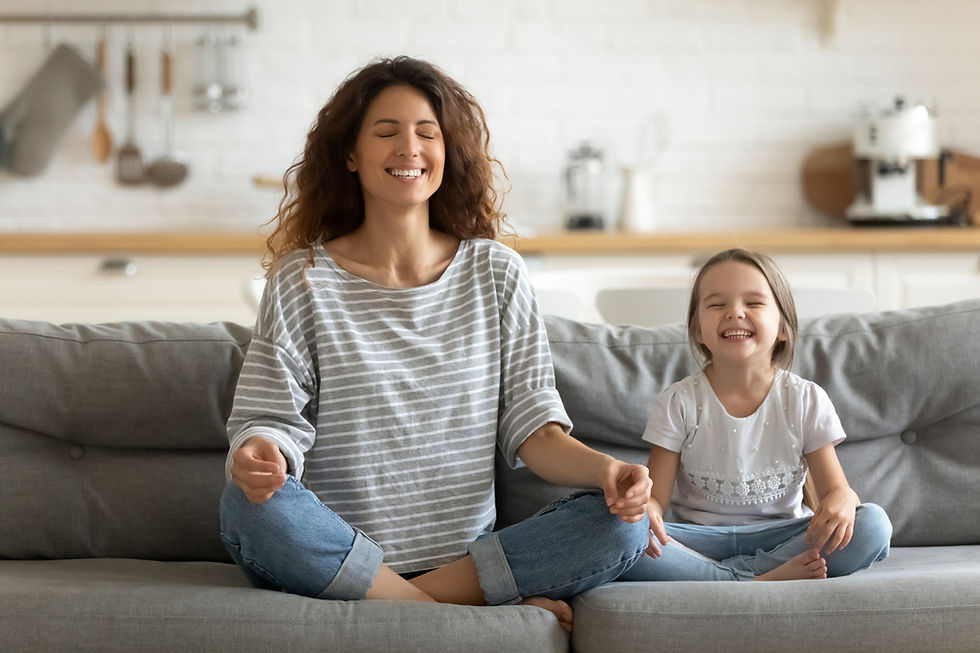 Full length happy young nanny mom sitting on sofa in lotus pose, teaching small daughter y