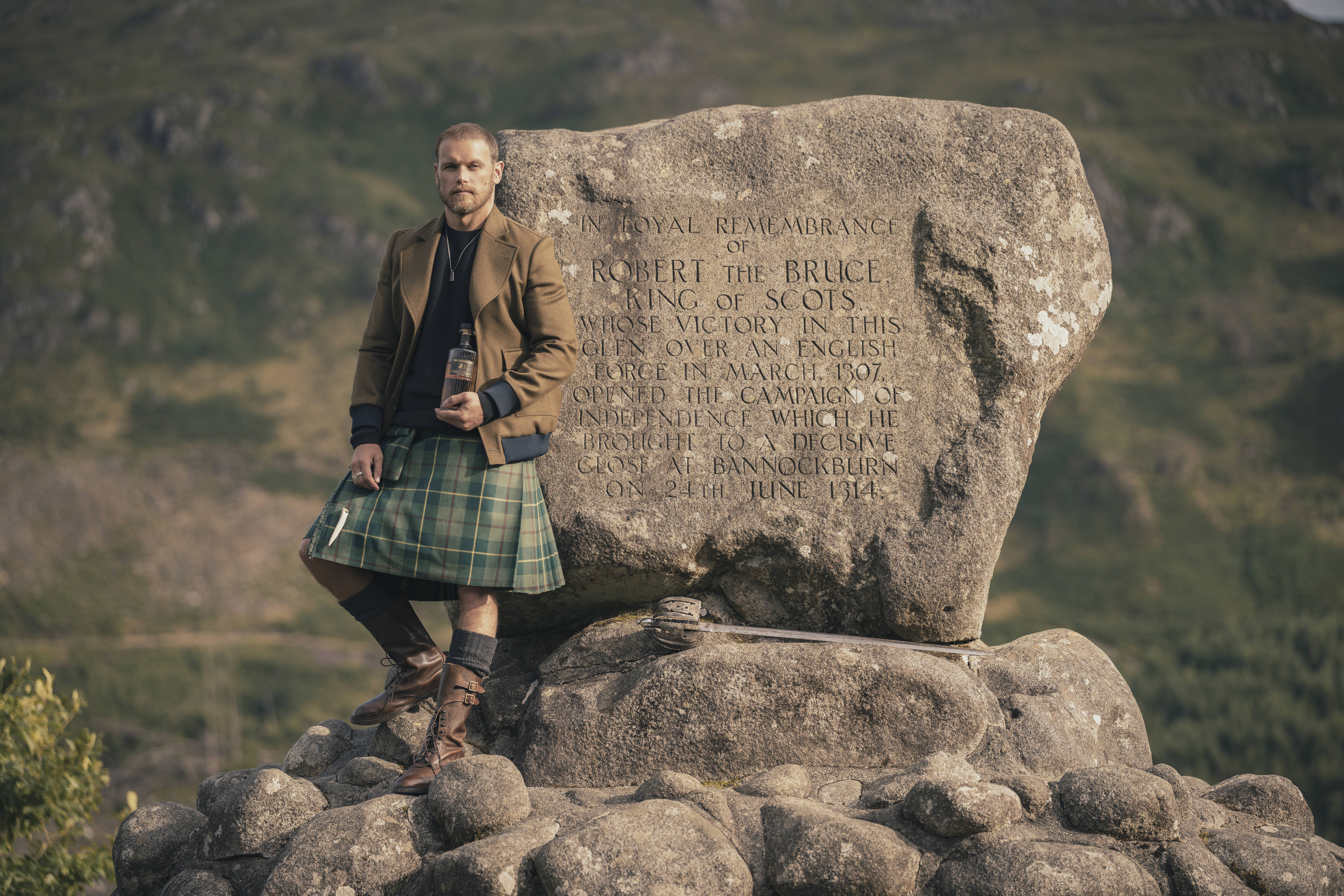 Sam Heughan in Scottish kilt next to Robert the Bruce monument.