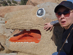 The author making a silly face while posed next to a painted rock that resembles a dog.
