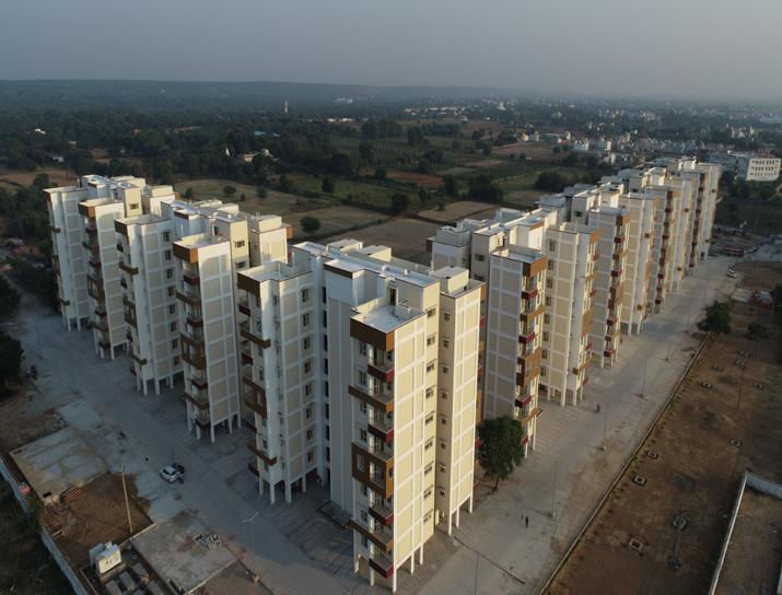 Aerial view of beige residential buildings with a rural landscape in the background. The sky is overcast, creating a calm mood.