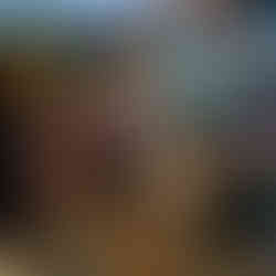 A man and a woman in a REAL School cap kneel side by side on straw mulch, planting a sapling together during the REAL Heartwoods community planting day in Graphisoft Park, Budapest, with a crowd of participants visible in the background.