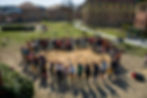 Over a hundred students, parents, teachers, and community members stand in a circle around the newly planted REAL Tiny Forest, arms raised in celebration, photographed from above in Graphisoft Park, Budapest, on community planting day, 14 March 2026. The heart-shaped mulched forest bed is visible at the centre of the group.