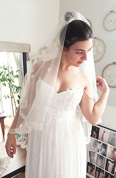 Dernier essayage à l’Atelier E : Margaux dans sa robe de mariée en mousseline de soie et son voile en organza de soie, fleurs en dentelle brodées à la main.