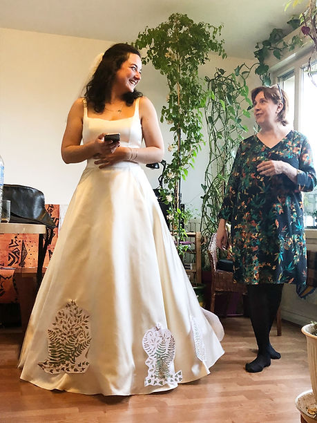 La mariée et l'artiste positionnent les motifs peints sur la robe lors d'un essayage à l'Atelier E.