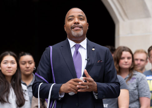 Man in suit speaking to a group outdoors.
