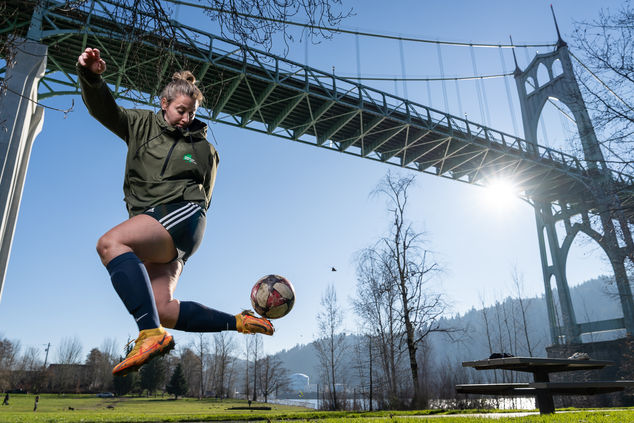 Person kicking soccer ball under bridge.