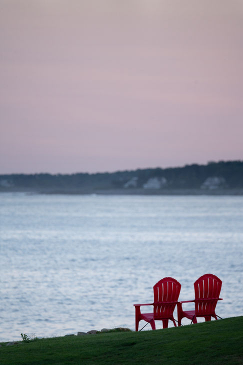 Two red chairs facing a calm, expansive sea.