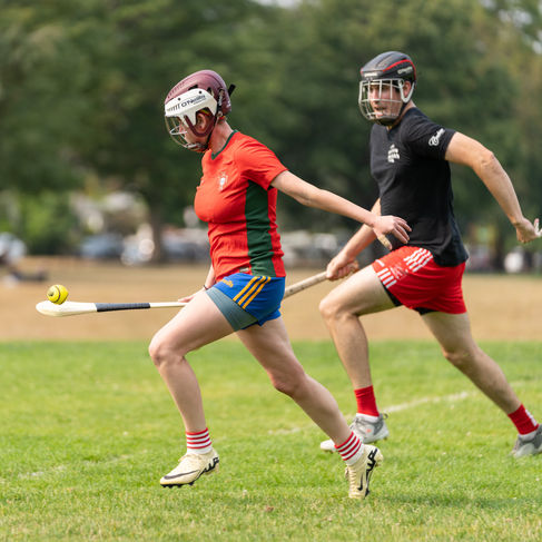 Two people playing hurling on a grassy field.