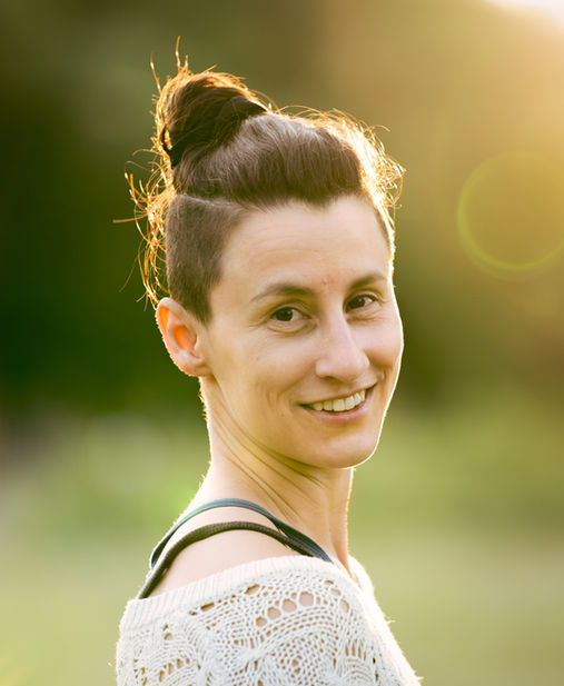 A person smiling outdoors with sunlight in background.
