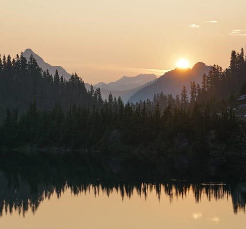 Sunset over mountains and forest reflected in lake.