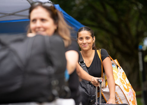 Two people outdoors, one smiling, carrying bags.