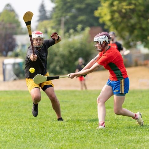 Two people playing hurling on a grassy field.