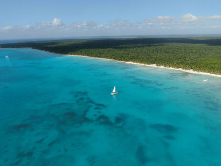 Aerial view of the turquoise Caribbean Sea and a white-sand coastline with a sailing boat – Caribbean cruise holiday from the UK