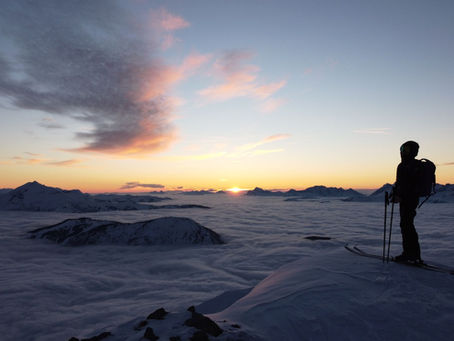 Skier standing on a snowy Alpine summit above the clouds at sunset – February half-term ski holiday inspiration
