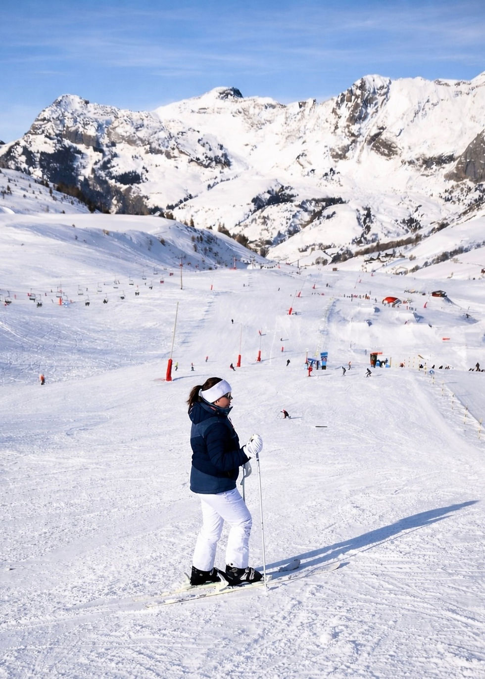 Skier on a sunny piste in the French Alps with snow-capped peaks behind – booking a February half-term ski holiday from the UK