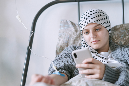 Young cancer patient receiving treatment while using a phone to contact her care team, symbolizing support and knowing who to call during cancer treatment