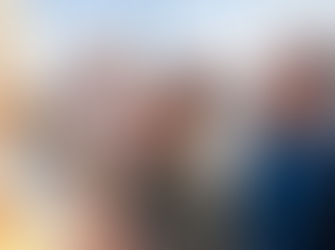 Smiling family with a mother holding her daughter in a colorful coat, chatting with grandparents outdoors on a sunny day by the seaside promenade.