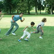 A family runs happily together across a grassy park on a sunny day, symbolizing outdoor play, joy, and healthy family time in nature.