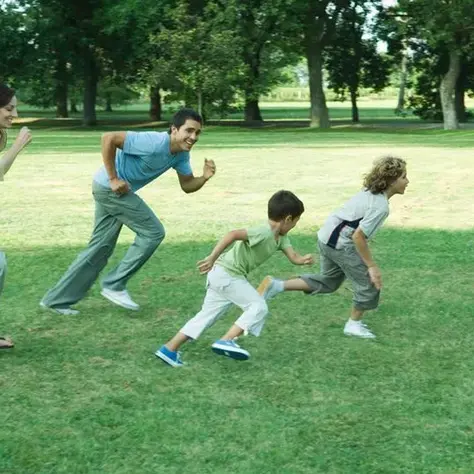 A family runs happily together across a grassy park on a sunny day, symbolizing outdoor play, joy, and healthy family time in nature.
