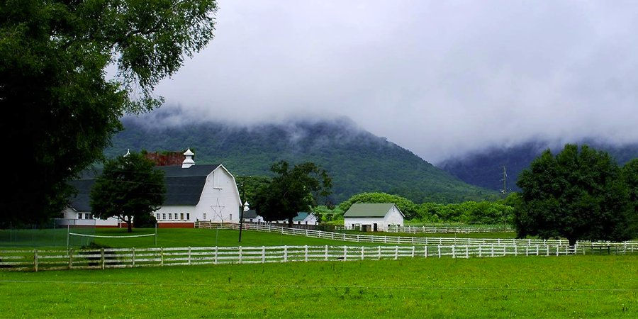 Scenic farmland with white barn and green fields, mountains partially obscured by clouds.