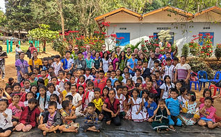 Jihad and a large group of people, including children and adults, pose together outdoors in front of colourful buildings.