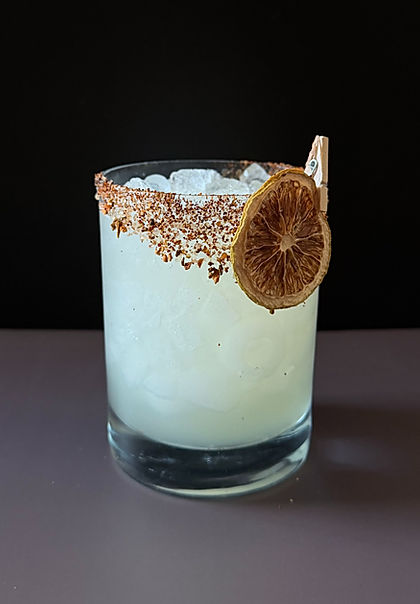 Tommy's Margarita in a rocks glass over crushed ice with a spicy salt rim and a dried lime wheel garnish, dark moody background.
