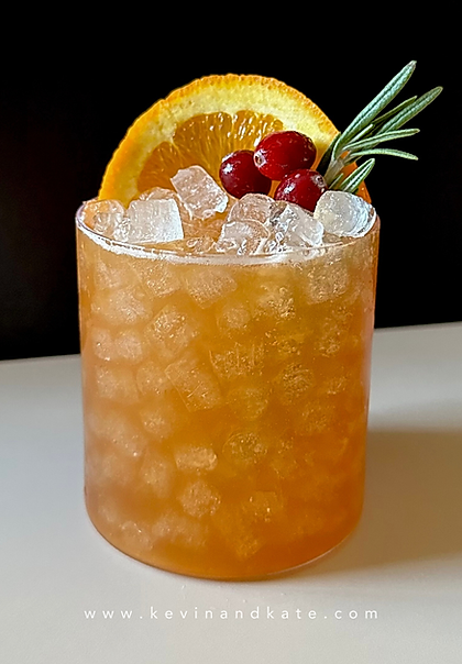 A Cranberry Orange Bourbon Smash served over crushed ice in a short glass, garnished with a rosemary sprig, orange slice, and fresh cranberries against a dark background.