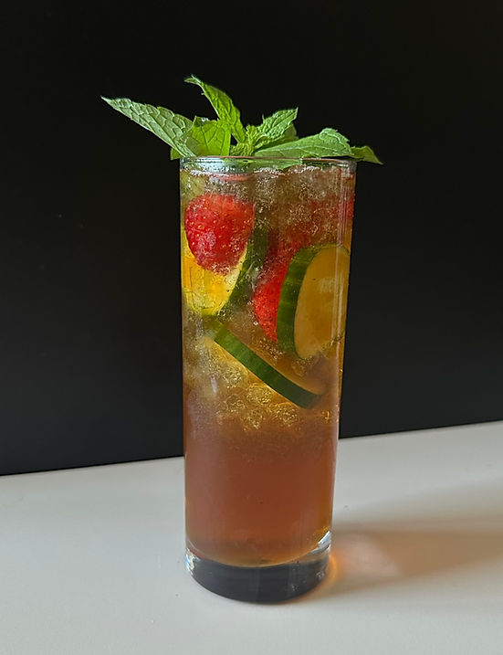 A tall wine glass filled with colorful Pimm’s Sangria, garnished with fresh strawberries, cucumber slices, lemon wedges, and a sprig of mint against a black background.