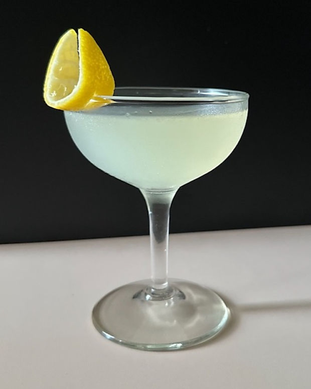 A bright Lemon Drop cocktail in a coupe glass, garnished with a fresh lemon twist against a dark background.