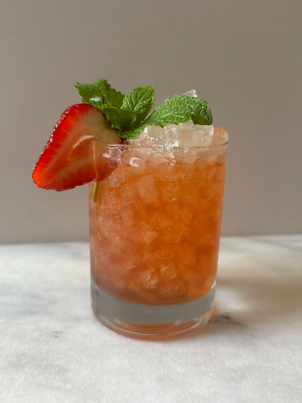 Rocks glass filled with strawberry bourbon smash, fresh herbs, and ice on a moody surface.