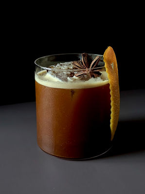 Pumpkin spice carajillo in a rocks glass with an expressed orange peel and star anise garnish, dark background.