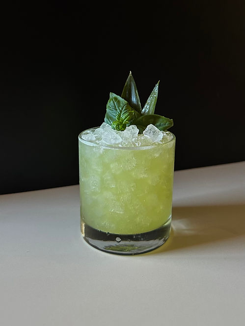 Bright green Pineapple Basil Smash cocktail in a high ball glass with pineapple fronds and a basil sprig.