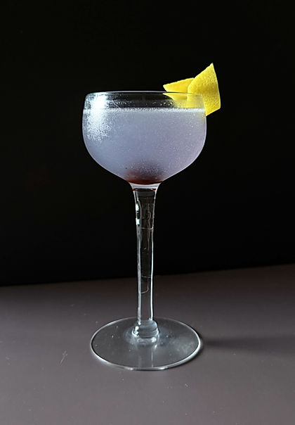 Aviation cocktail in a chilled coupe glass with a soft lavender hue, garnished with a lemon twist, dark moody background.