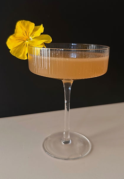 An Earl Grey tea mocktail served in a coupe glass, garnished with a yellow edible flower, set against a dark background.