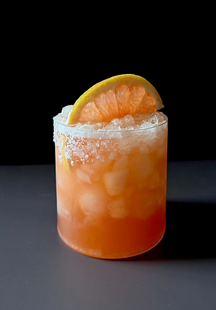 Grapefruit Aperol Margarita in a rocks glass over crushed ice with a Tajín rim and a fresh grapefruit slice garnish, dark moody background.