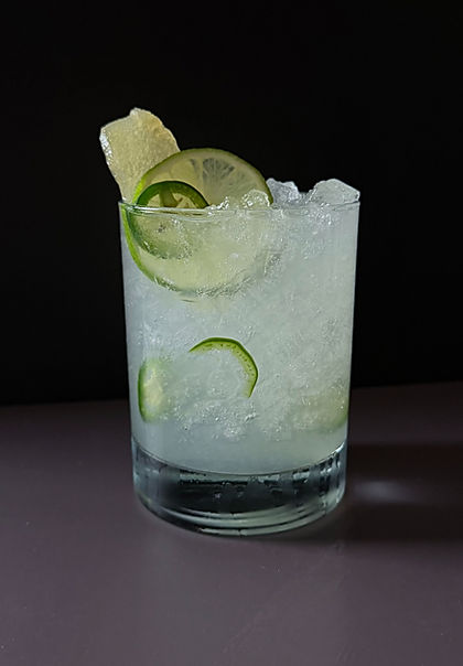 Spicy Ginger Mule in a rocks glass over crushed ice, garnished with jalapeño rounds, a lime wheel, and candied ginger on a dark background.