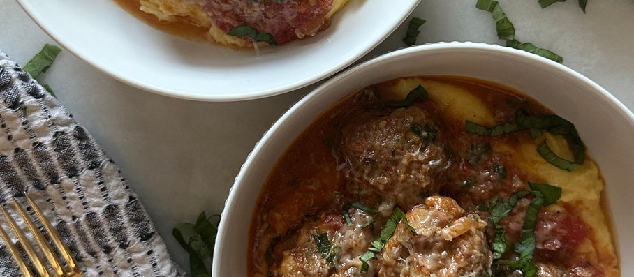 Plated summer meatballs in fresh tomato sauce over creamy polenta with basil.