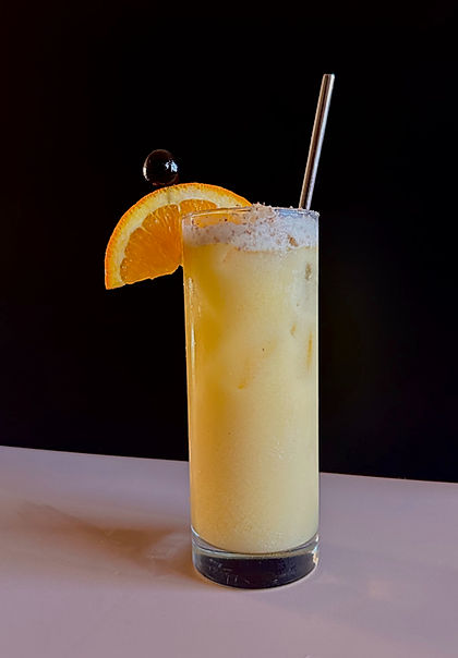A Painkiller cocktail served in a tall glass with a salted rim, garnished with an orange wheel and cherry, with a metal straw.