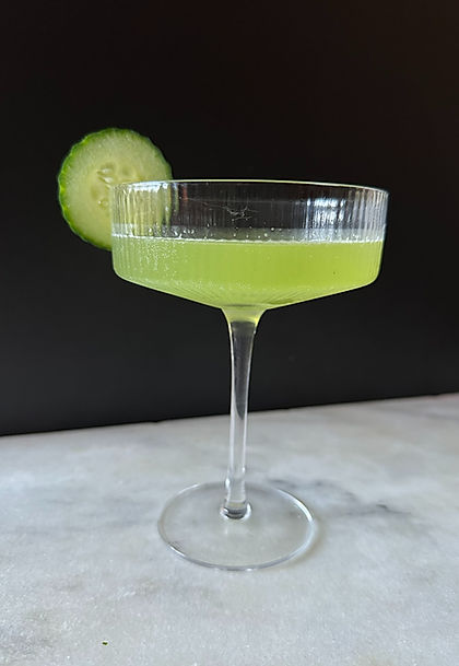 Cucumber martini served in a coupe glass with fresh cucumber garnish on a marble surface against a dark background.